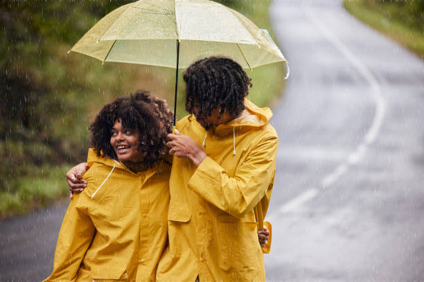 Happy black couple walking embraced under umbrella on rainy day.