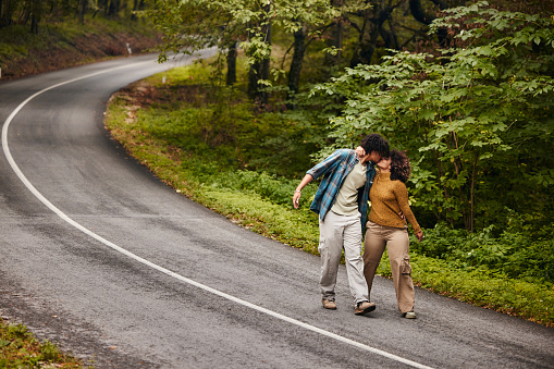 Affectionate African American couple kissing while walking on empty road in autumn day. Copy space.