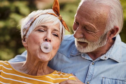 Carefree senior woman blowing a bubble from a gum while spending a day with her husband outdoors.