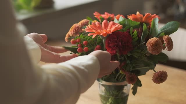 Putting vase with orange flowers on wooden table by female hands, slow motion