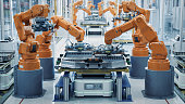 EV Battery Pack Automated Production Line Equipped with Orange Advanced Robot Arms. Row of Robotic Arms inside Bright Plant Assemble Batteries for Automotive Industry. Modern Electric Car Smart Factory.