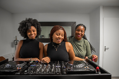 Two Black teenage female DJs and their mother practising at home for a performance