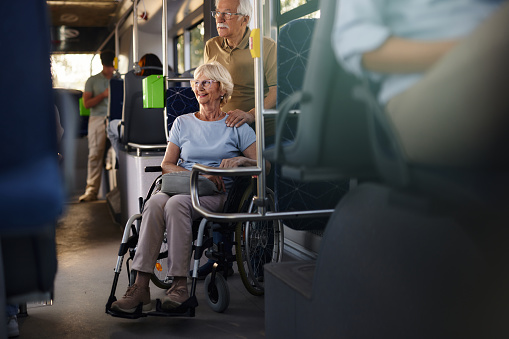 Happy disabled senior woman in a wheelchair and her husband traveling by a bus.