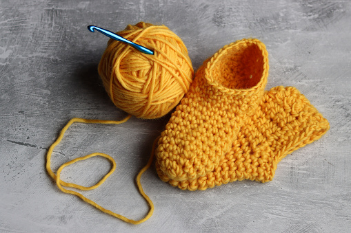 Knitted baby booties and ball of yellow wool on a gray background with copy space. Handmade slippers close up photo.