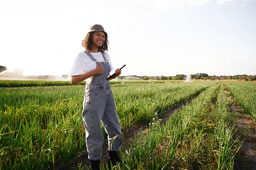 Smiling woman farmer work on digital tablet standing on field. Agricultural business concept