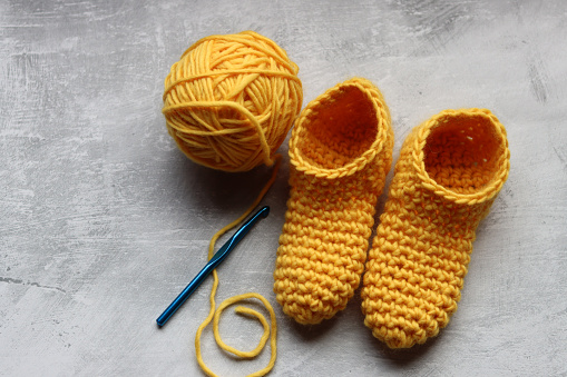 Knitted baby booties and ball of yellow wool on a gray background with copy space. Handmade slippers close up photo.