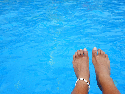 Feet adorned with a bracelet on the edge of a pool near the water