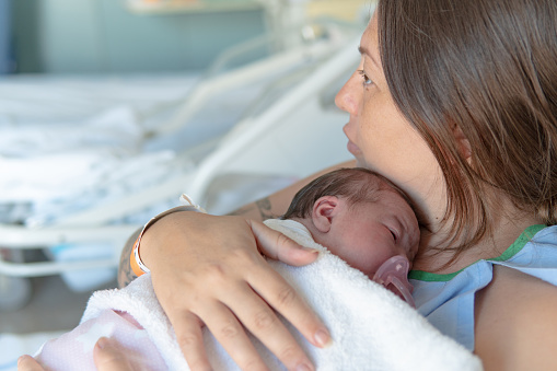 Close up of mother holding a sleeping newborn baby in the bed of a hospital room. Healthcare medical love woman lifestyle mother's day, breast concept with copy space