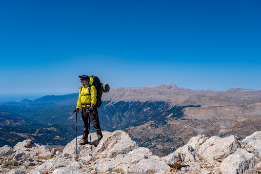 65 years old fully equipped hiking man. With a backpack, walking sticks and walking shoes. At high altitudes. It has high viability. Mediterranean region mountain ranges, extremely steep terrain. High altitude. Light blue air.