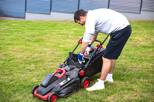 A man uses an electric lawnmower