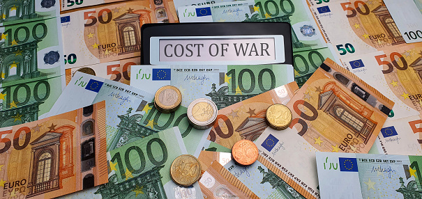 The cost of war. A calculator surrounded by euro bills and coins. The concept of militarization, increased spending on weapons for defense, the army, military training, the fight against terrorism