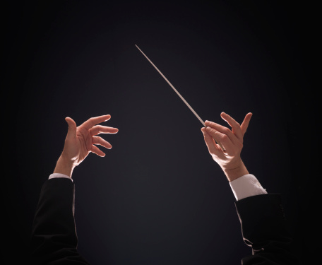 Concert conductor hands with baton over dark background
