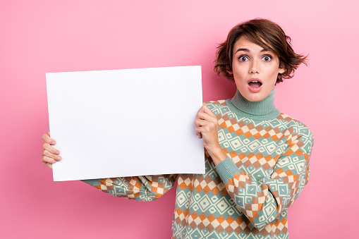 Portrait of young girl black friday purchase shopaholic holding paper promo billboard shock speechless isolated on pink color background.