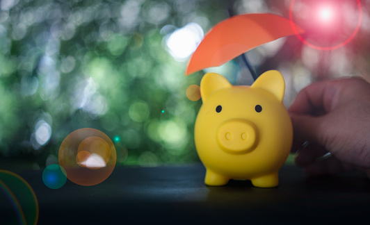 Man hand hold the orange umbrella for protect to a yellow piggy bank. Risk insurance in banking.