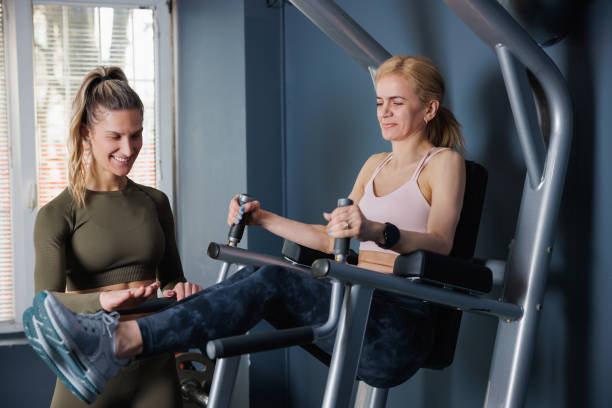 istock Woman using exercise equipment in the gym, her instructor smiling and assisting 1733393118