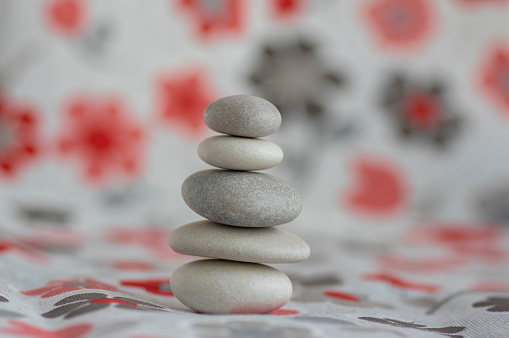 Stone cairn on white background with red and gray flowers stars, five stones tower, simple poise stones, simplicity harmony and balance, rock zen