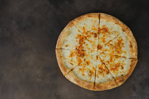Slices of fresh round pizza with saucages, cheese on dark brown background, top view. High quality photo