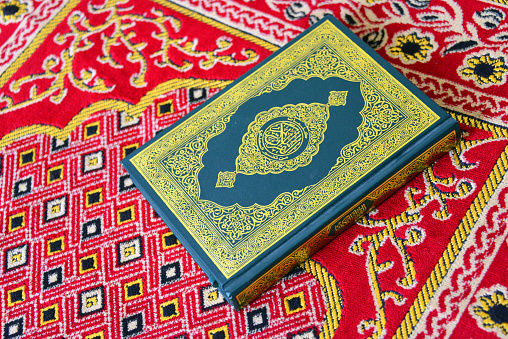Salalah, Dhofar Governorate, Oman: Holy Quran / Koran on a Prayer Rug - Ornate cover, richly decorated with golden floral motives and Arabic calligraphy.