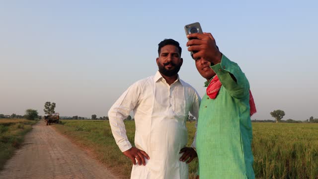 Indian farmer taking selfie near green field during springtime
