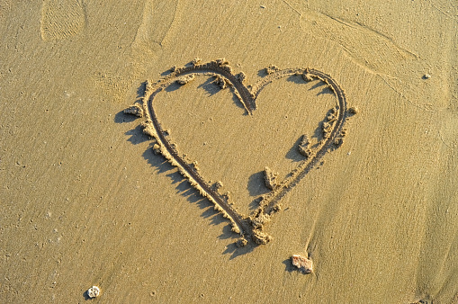 a picture of a heart carved into the beach sand which symbolizes love