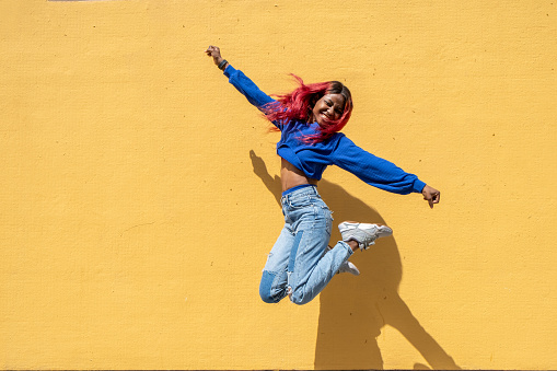 Portrait of a cool african american young woman jumping outdoors in a yellow background