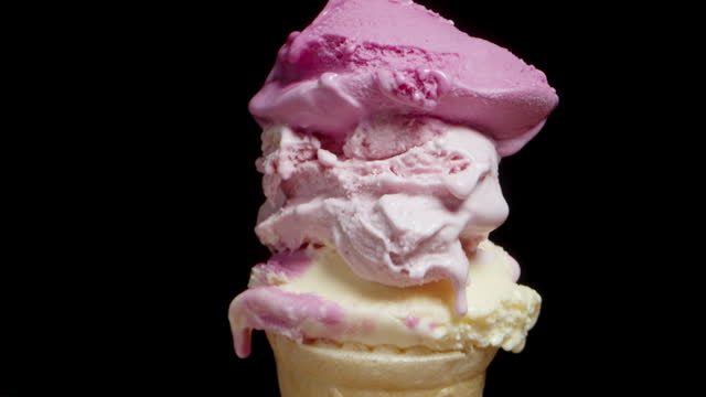 Waffle cone with three scoops of pink ice cream on the table against a black background, close-up, with a tilt effect.