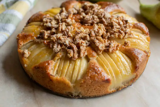 Delicious and juicy homemade pear cake with caramelized walnut topping. Served whole and ready to eat isolated on light background. Closeup