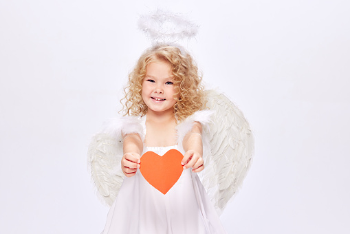 Banner for Valentine's Day. Angel girl with real gift, studio portrait. Playful angelic little girl. Concept of gift and celebration. Cupid's little child.