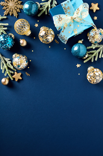 Blue and gold luxury Christmas balls ornaments, glitter blue paper gift box, fir branches on dark blue background. Xmas vertical banner design, Happy New Year party invitation card template.