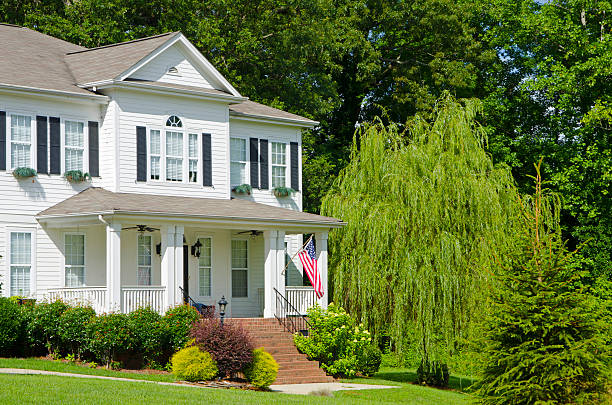 A American flag hanging outside a home. An American Flag hangs from the front porch of this Victorian-style home in honor of the upcoming Holiday Celebration. A mature Weeping Willow tree grows next to the home. weeping willow stock pictures, royalty-free photos & images