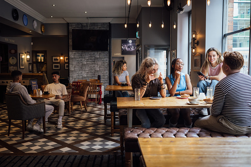 A wide shot of a multiracial group of students in a pub in Newcastle Upon Tyne. They are sitting at a table, talking and relaxing with drinks and food.