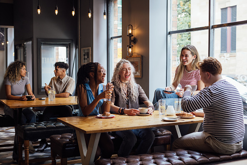 A wide shot of a multiracial group of students in a pub in Newcastle Upon Tyne. They are sitting at a table, talking, laughing and relaxing with drinks and food.