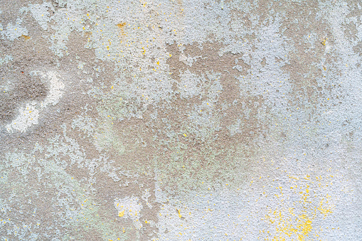 Flaking yellow white paint on the stucco exterior wall of an old house