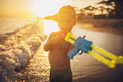Little boy with squirt gun standing on the beach in the sea.