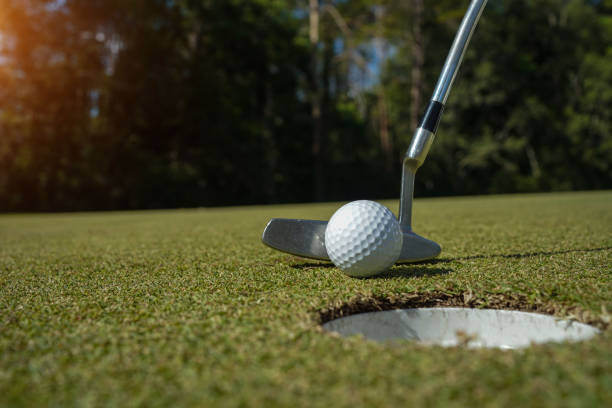 グリーン上にゴルフボールを置くゴルファーの練習トレーニング、夕方の太陽の上にレンズフレア - golf green practicing sports training ストックフォトと画像