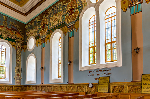 Kutaisi, Georgia, 04.06.21. Kutaisi Synagogue inside view of richly decorated side wall and wooden benches, colorful paintings on Synagogue wall.