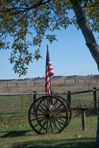 Old weathered and broken wagon or cart wheel with United States flag attached in Montana in western USA of North America.