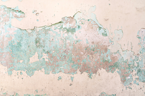 Flaking turquoise blue paint on the stucco exterior wall of an old house