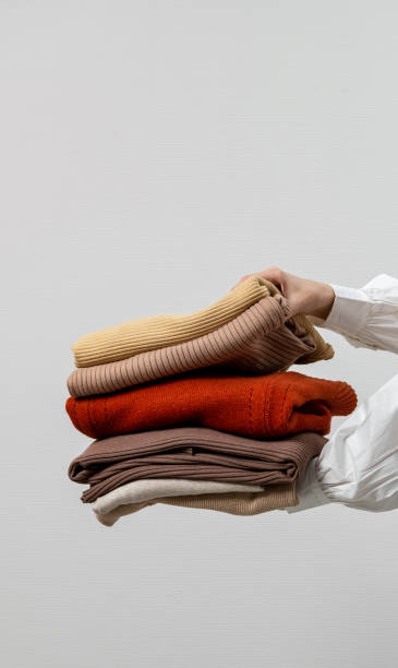 istock Woman hands holding stack warm winter sweaters on grey background. A stack of sweaters, jumpers in female hands. Winter and autumn warm cozy sweaters for charity. 1733670755