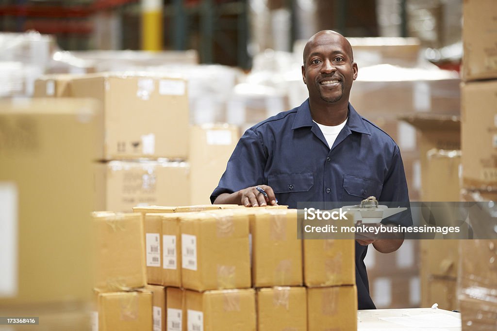 A worker in a warehouse preparing goods for delivery Worker In Warehouse Preparing Goods For Dispatch Smiling To Camera Warehouse Stock Photo