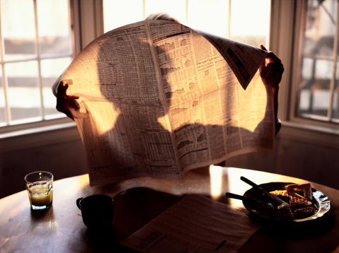 Person reading a newspaper with their shadow showing.thru with the morning sunlight...