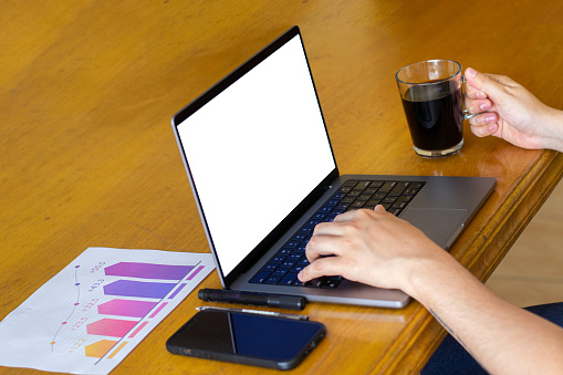 A person diligently working on a laptop computer, with a steaming cup of coffee by their side. The laptop's screen is aglow with the soft light of the display, highlighting the person's focused engagement with the tasks at hand. The coffee, in a warm and inviting container, adds a touch of comfort and refreshment to their work environment