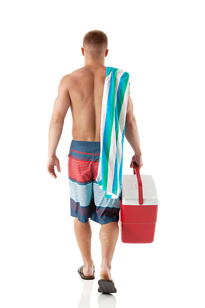 rear view of a с открытой грудью человек ходить с холодильник - male swimwear cooler 20s стоковые фото и изображения