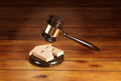 Gavel hitting a house shaped wooden piece on a sounding block on a wooden table. Illustration of the concept of housing legal issues