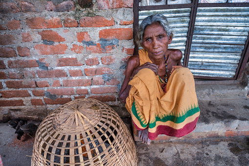 Elderly woman from the Indian region of Odisha at the door of her house with a basket of chickens