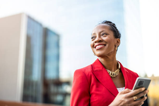 portrait of smiling mature businesswoman using mobile phone in urban setting - affärsmänniska bildbanksfoton och bilder