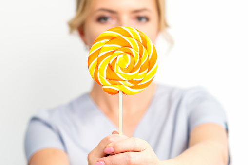Beautiful young woman holding colorful lollipop candy in hand having fun over yellow background. Sweet food and happiness concept.