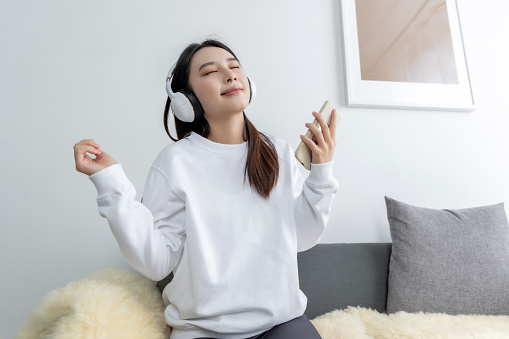 Music Enthusiasm: Young Asian Woman at Home, Swinging to the Rhythm with Headphones and Mobile Phone