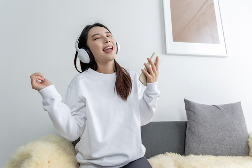 young pretty Asian girl sitting on a cozy sofa in the living room while listening the music