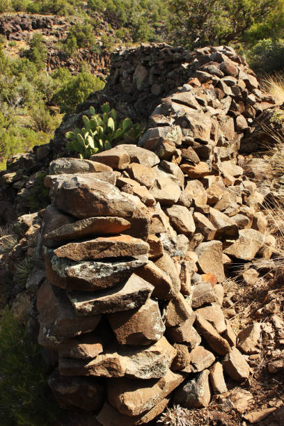 Volcanic rock stacked atop existing boulders to form an exterior cliff dwelling wall.  The Sinagua Indian tribe that selected this site did so for its position atop a high desert promentory.  On the opposite side of the site a sheer cliff drops to a long steep hill that descends to a dry riverbed - allowing no access from that side.  This wall includes small portals where rocks were omitted so that arrows could be fired through them, permitting concealment from enemy attack.  The wall has only one entrance opening and visibility is good for hundreds of yards.  Site selection was critical for the Sinagua, and perfectly executed here. This culture combined hunting and gathering with agriculture, but the latter was challenging in this arrid, high desert wilderness terrain. The exact site location, which requires considerable effort to reach, is intentionally omitted.  Its estimated age dates to 1300 AD - 1400 AD.  Remote Sinagua Cliff Dwelling Site, Northern Arizona, 2013.